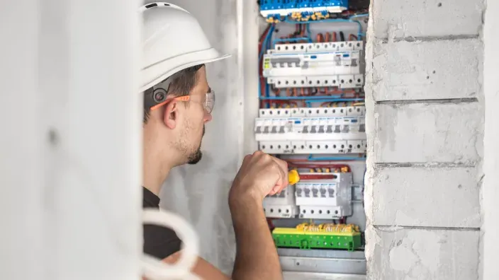 Técnico con casco trabajando en un cuadro eléctrico con un destornillador