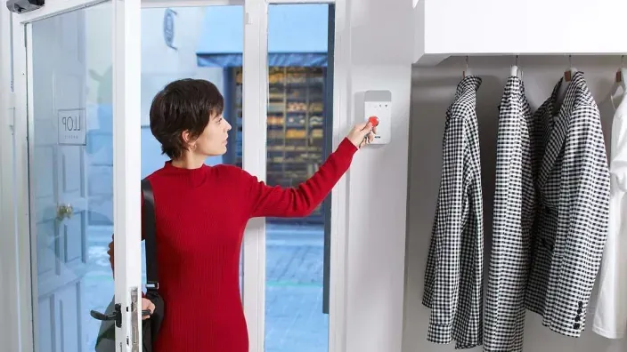 Mujer entrando en un local comercial y desactivando el sistema de alarma en la pared.