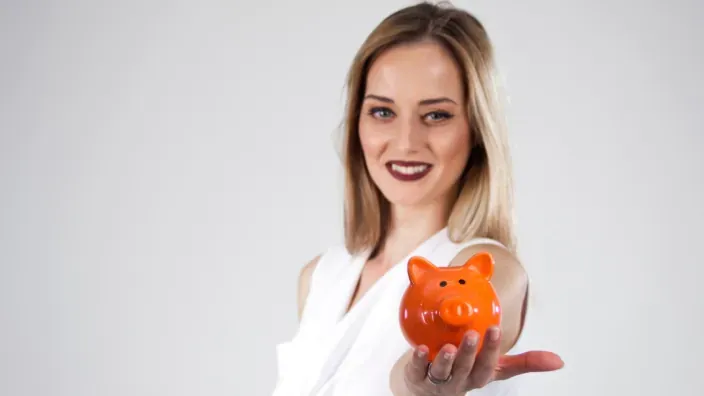Mujer sosteniendo una hucha naranja en la palma de su mano como símbolo de ahorro y finanzas personales.