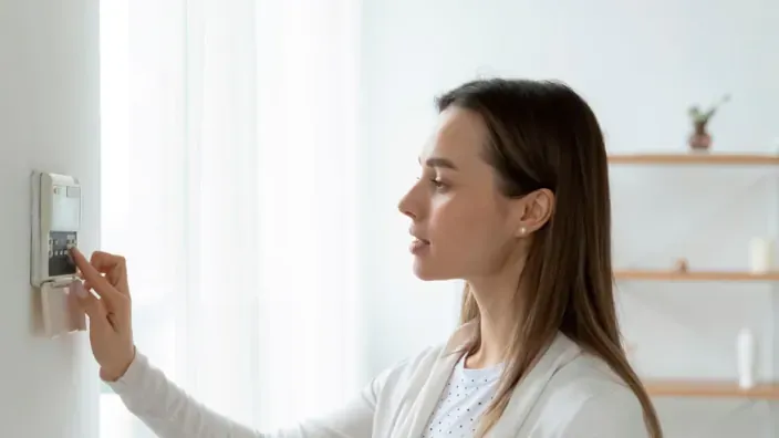 Mujer joven ajustando su alarma de seguridad doméstica,