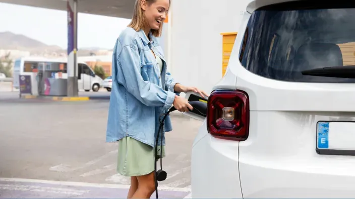 Mujer cargando un coche eléctrico en una estación de recarga pública