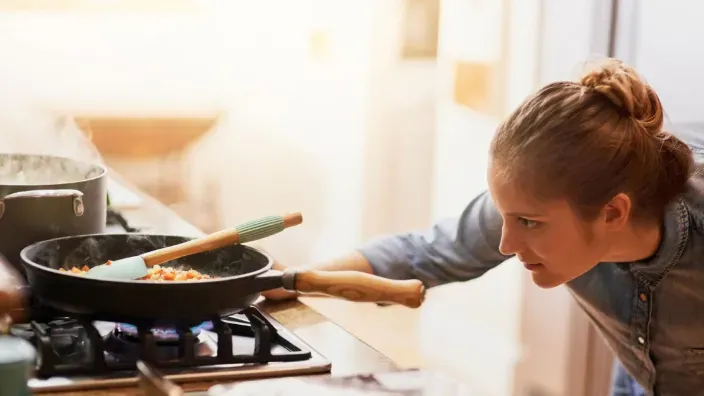 Mujer cocinando y controlando sartén en el fuego de la cocina de gas con utensilios.