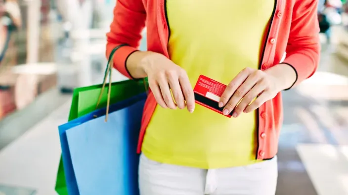 Mujer de compras en tienda física sosteniendo tarjeta de crédito roja y bolsas de colores.