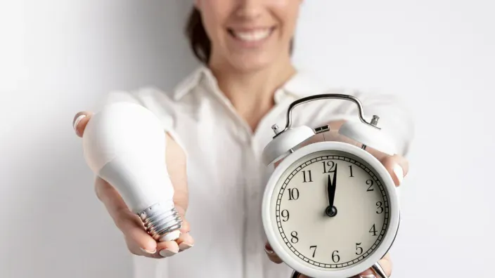 Mujer sonriente sosteniendo una bombilla y un reloj en cada mano
