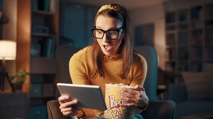 Mujer sentada en un sillón con una tablet y un cubo de palomitas