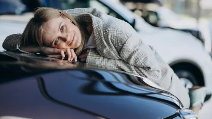 Mujer feliz abrazada al capó de su coche nuevo en un concesionario tras contratar un seguro de coche.