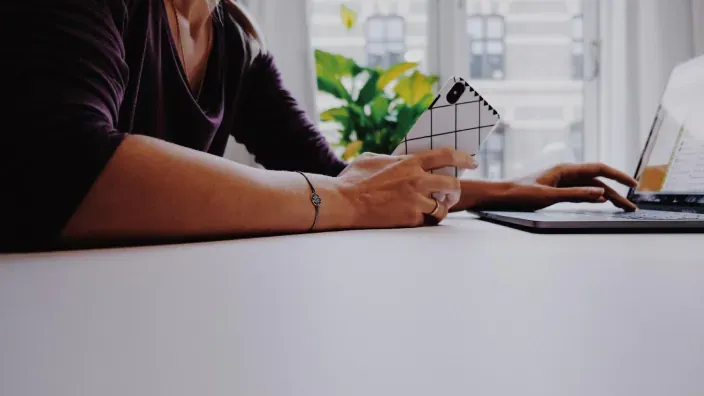 Mujer en casa usando el portátil y el móvil para gestionar gastos y finanzas personales