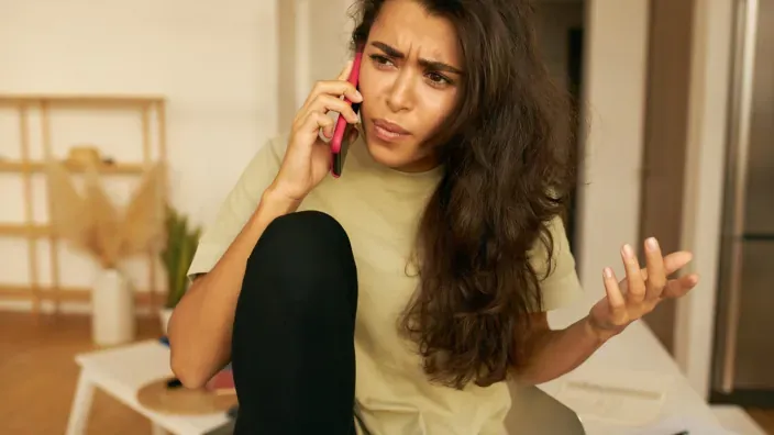 Mujer joven hablando por teléfono con expresión de preocupación en el interior de una vivienda.