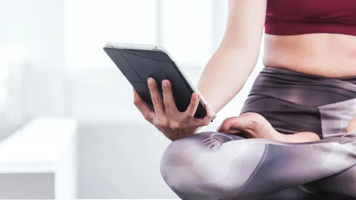 Mujer practicando yoga con tablet en la mano siguiendo clase online de fitness o meditación.