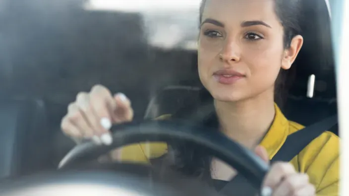 Primer plano de mujer joven concentrada conduciendo con las manos en el volante y cinturón puesto.
