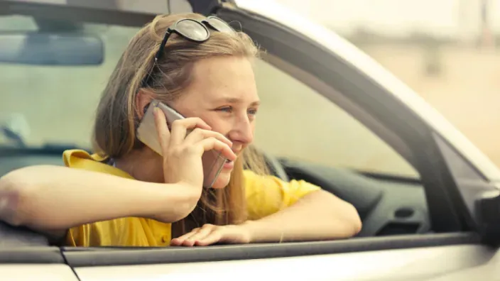 Mujer joven hablando por teléfono desde la ventanilla de su coche en un día soleado.