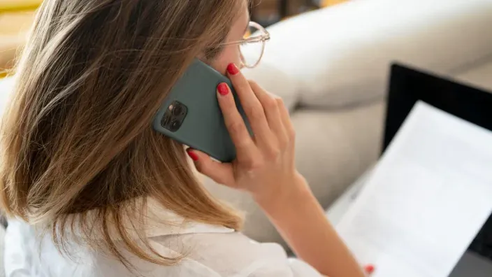 Mujer hablando por teléfono mientras sostiene una factura en casa.