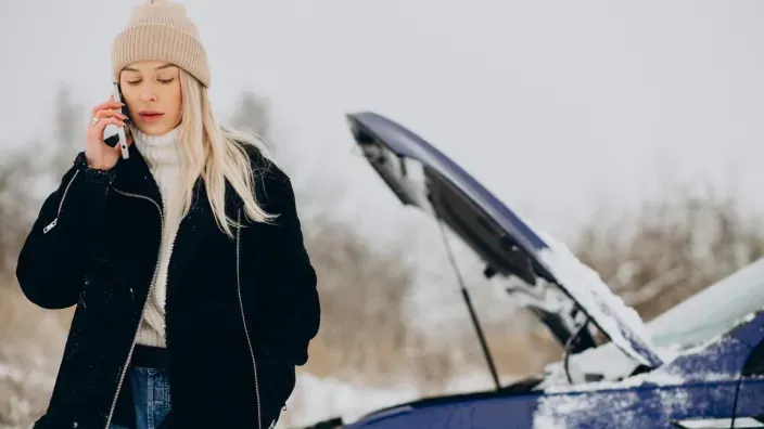 Mujer llamando por teléfono junto a su coche averiado en medio de la nieve.