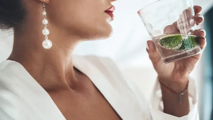 Mujer elegante con pendientes de perla sosteniendo un vaso con lima.
