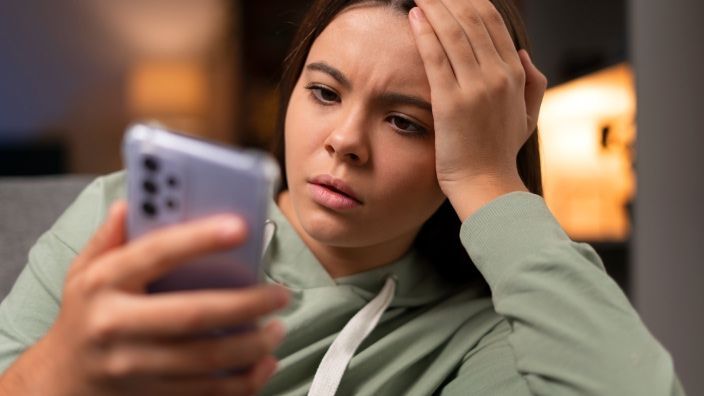 Adolescente preocupada mira su móvil. Símbolo del ciberacoso (bullying) y su impacto en la salud mental de los jóvenes.