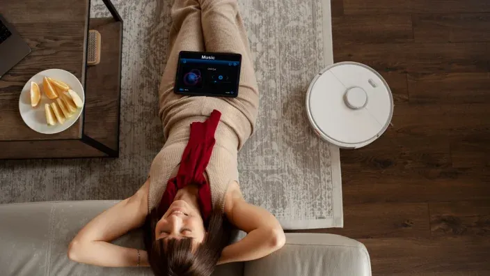 Mujer relajada en casa mientras un robot aspirador limpia el suelo.