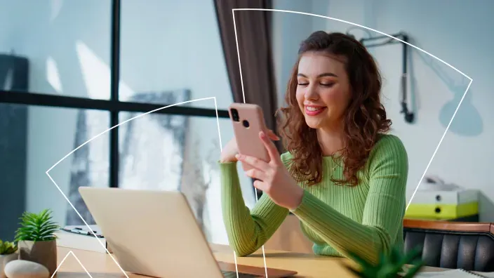 Mujer joven sonriendo mientras usa su smartphone y portátil.