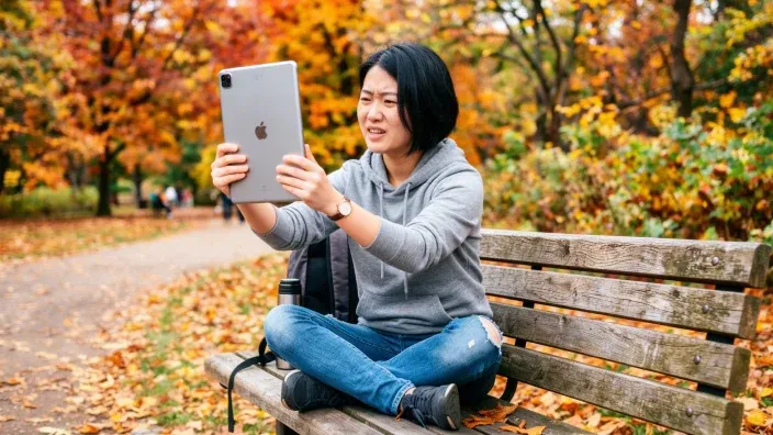 Mujer confundida usando un iPad en un parque para representar errores de funcionamiento o compatibilidad en tablet.
