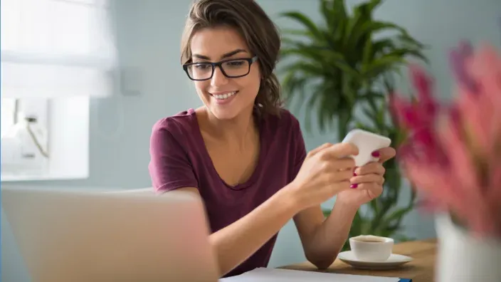 Mujer joven trabajando desde casa con portátil y móvil, reflejando la digitalización de los servicios de seguros.