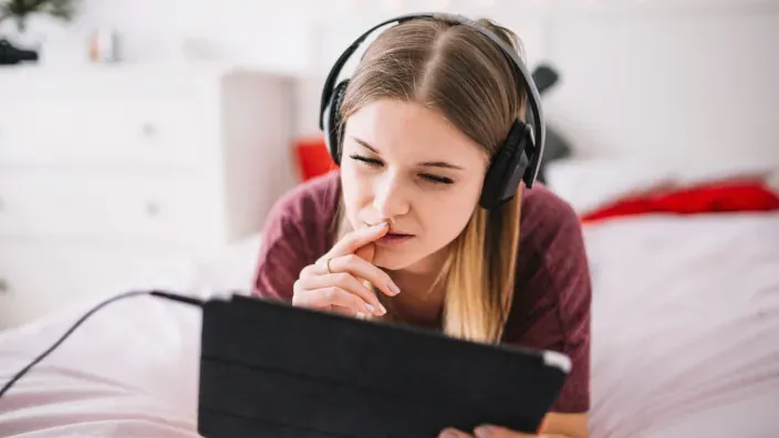 Joven con auriculares viendo una tablet en su dormitorio, reflejando el consumo de contenido digital en casa.