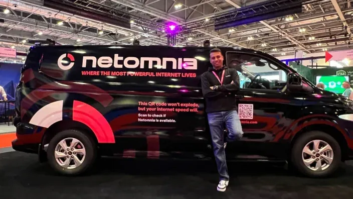 Representante de Netomnia posando junto a furgoneta rotulada de internet en una feria.