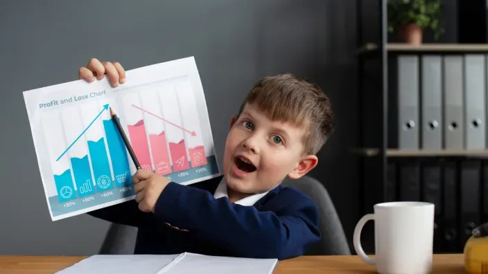 Niño vestido de traje mostrando una hoja con un gráfico de ganancias y pérdidas mientras señala las barras con entusiasmo.
