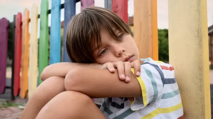 Niño triste y solo en el patio del colegio. Símbolo de la soledad, la salud mental infantil o el posible acoso escolar (bullying).