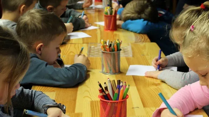 Grupo de niños pequeños dibujando y coloreando en clase alrededor de una mesa de madera