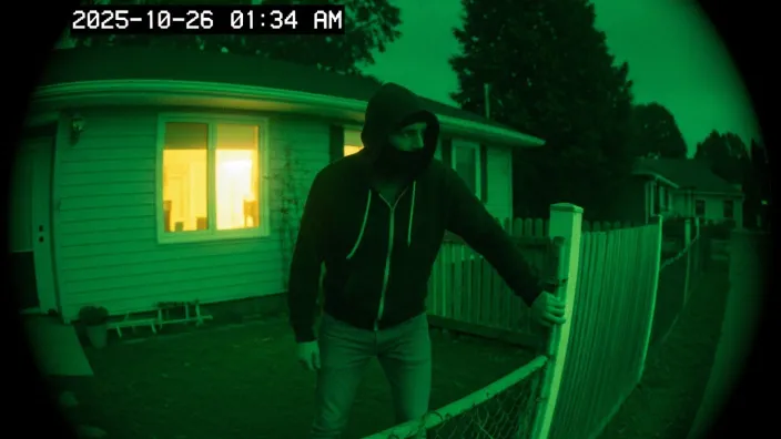 Imagen de cámara de seguridad con visión nocturna captando a un ladrón con capucha intentando saltar una valla