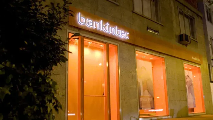 Exterior de una oficina de Bankinter de noche con el logo iluminado.