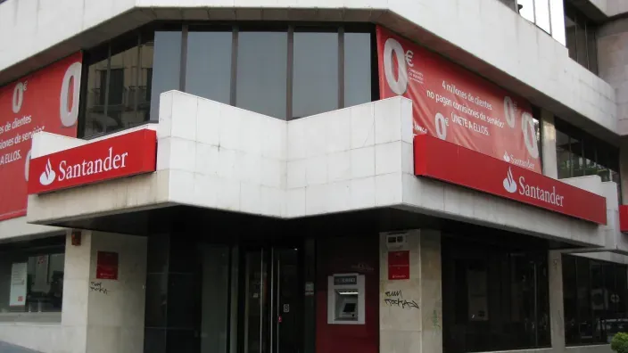 Fachada de una oficina o sucursal del Banco Santander a pie de calle, con sus logos y un cajero automático.