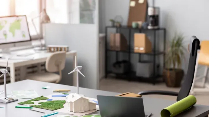 Oficina de diseño sostenible con maqueta de vivienda ecológica, mini aerogenerador y materiales de planificación ambiental.