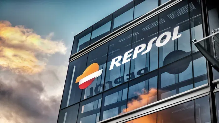 Fachada acristalada del edificio de Repsol con su logotipo visible y el cielo nublado al fondo.