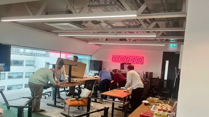 Oficinas de Monzo en construcción con el logotipo de neón y equipo trabajando en la sede del neobanco.