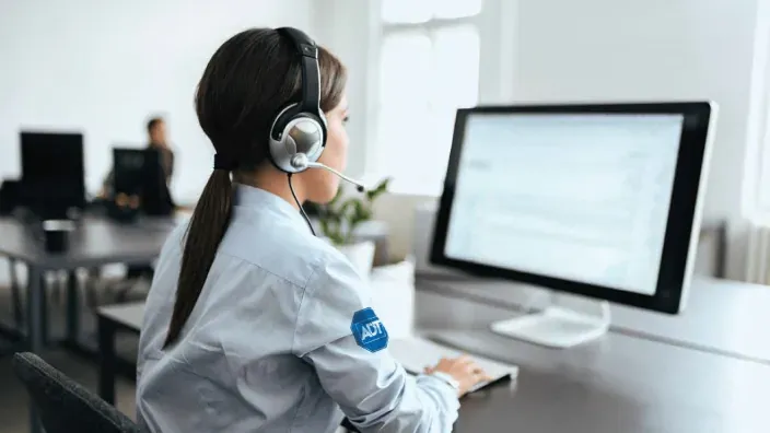Operadora de ADT con auriculares en una central receptora de alarmas para vigilar la seguridad de hogares y negocios