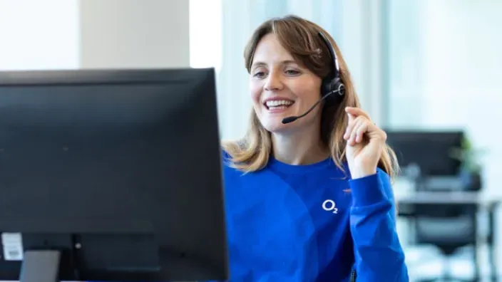 Operadora de atención al cliente de O2 con auriculares resolviendo dudas técnicas desde su puesto de trabajo.