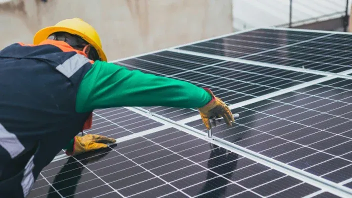 Técnico con casco trabajando en la instalación de paneles solares sobre una cubierta.