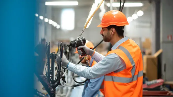 Operario con casco naranja y chaleco reflectante trabajando en un panel de control industrial