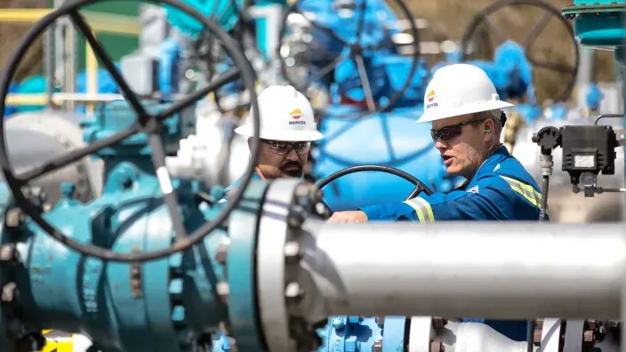 Técnicos con casco trabajando en una instalación industrial de gas con tuberías y válvulas de gran tamaño.