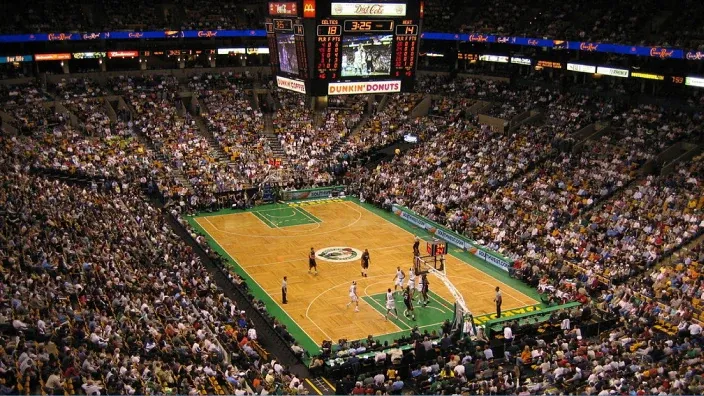 Pabellón de la NBA lleno durante un partido con la pista iluminada y las gradas abarrotadas de aficionados.