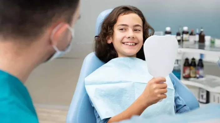Niña sonriendo y mirándose en un espejo en la consulta del dentista tras una revisión o tratamiento dental.