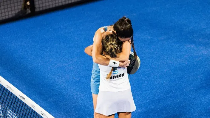 Las jugadoras de padel Jensen e Icardo se abrazan en la red tras un partido en pista azul.