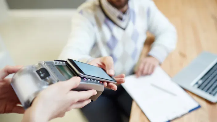 Hombre realizando un pago contactless con su móvil en un datáfono. Tecnología de pago móvil NFC y transacciones seguras.