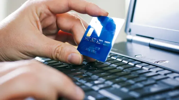 Primer plano de una mano introduciendo los datos de una tarjeta de crédito en un portátil para realizar una compra o pago online.