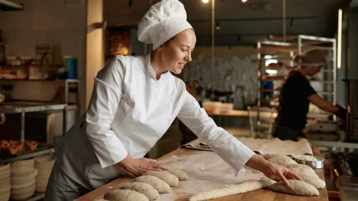 Panadera con uniforme blanco colocando piezas de masa sobre una mesa de trabajo