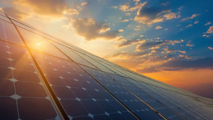Paneles solares fotovoltaicos iluminados por el sol al atardecer con cielo parcialmente nublado.
