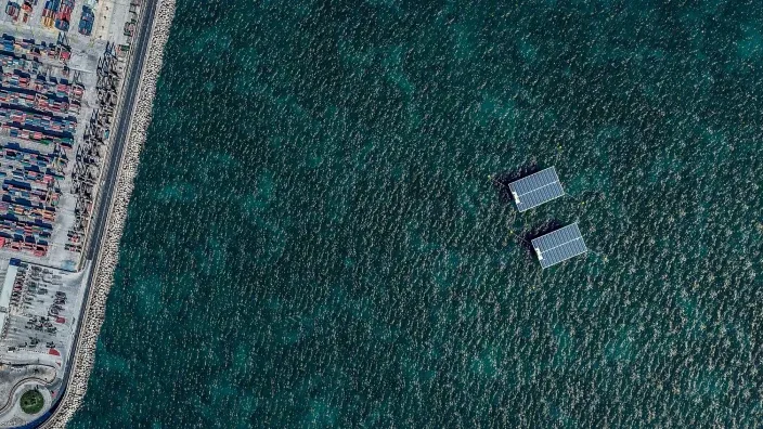 Vista aérea de dos estructuras de paneles solares flotantes situadas junto al puerto y el rompeolas.