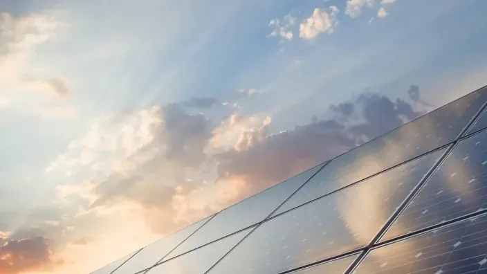 Placas solares fotovoltaicas captando energía renovable bajo un cielo de atardecer nublado.