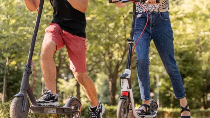 Pareja paseando en patinetes eléctricos por un parque.