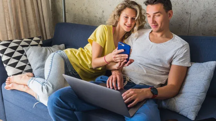 Pareja usando el móvil y un portátil para comparar precios y hacer compras online.